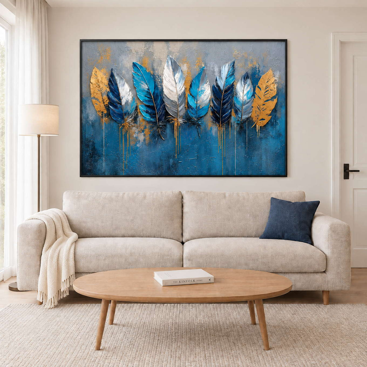 Blue, white and gold feathers against a deep blue and gray background in a black frame, displayed above a sofa in a living room.