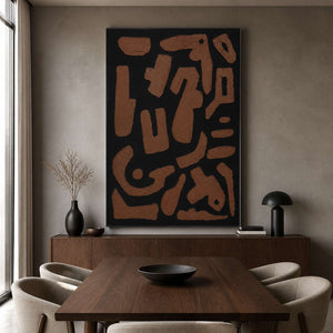 Black framed earthy abstract painting beside a wooden dining table.