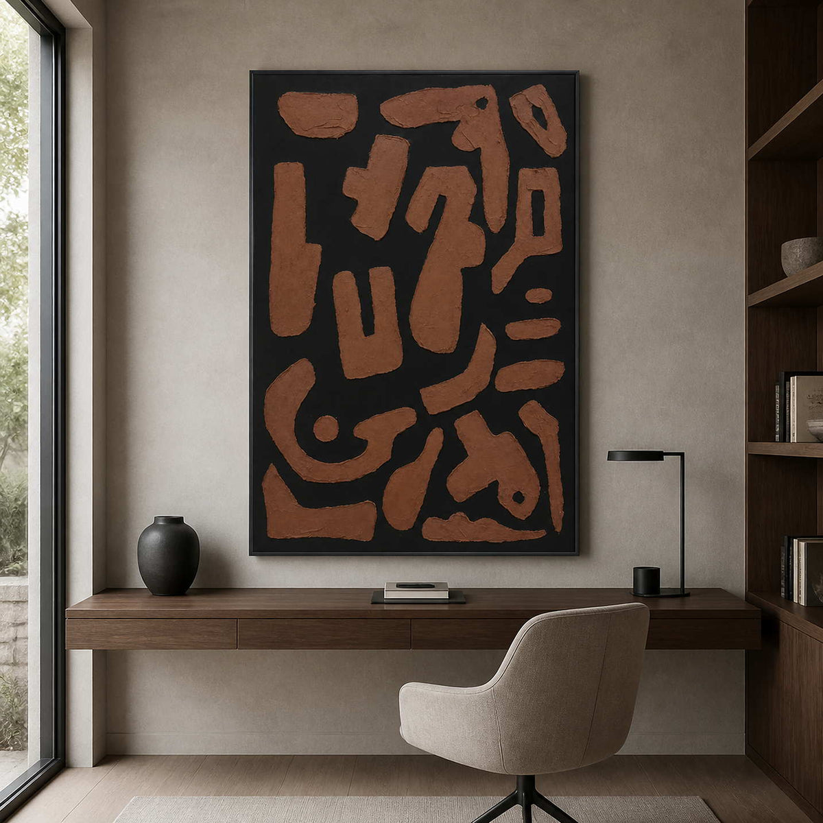 Black framed earthy abstract painting above a window lit home study desk.