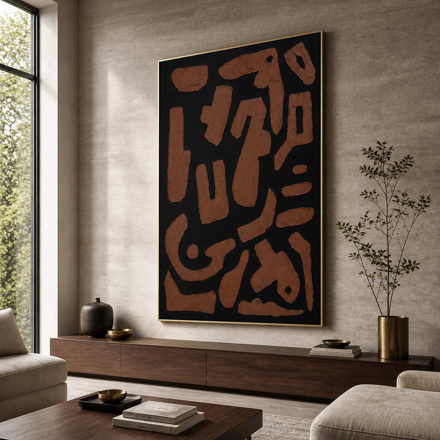 Gold framed rust and black abstract painting beside seating in a sunlit living room.