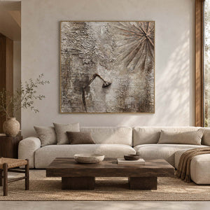 In a living room above seating, an artwork with a gold-colored frame shows gray-beige grid textures, radiating grooves and a dark bent raised line.