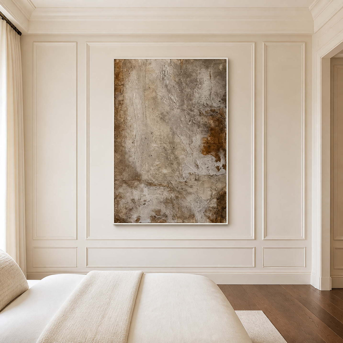 White framed weathered neutral artwork beside a cream bed in a quiet bedroom.