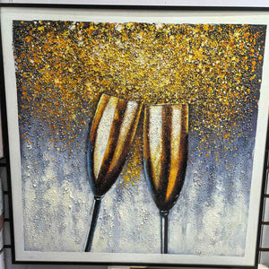 Photographed view of two golden champagne flutes leaning together beneath gold-colored speckles on blue gray, with the artwork edge and surrounding background visible.