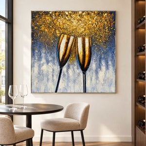 Beside a small tasting table and bottle shelving, an artwork with a silver-colored frame shows two golden champagne flutes leaning together beneath gold-colored speckles on blue gray.