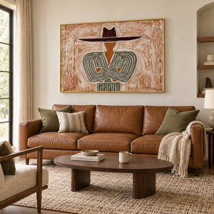 Effortless Poise in a gold frame above a brown leather sofa with olive and striped cushions.