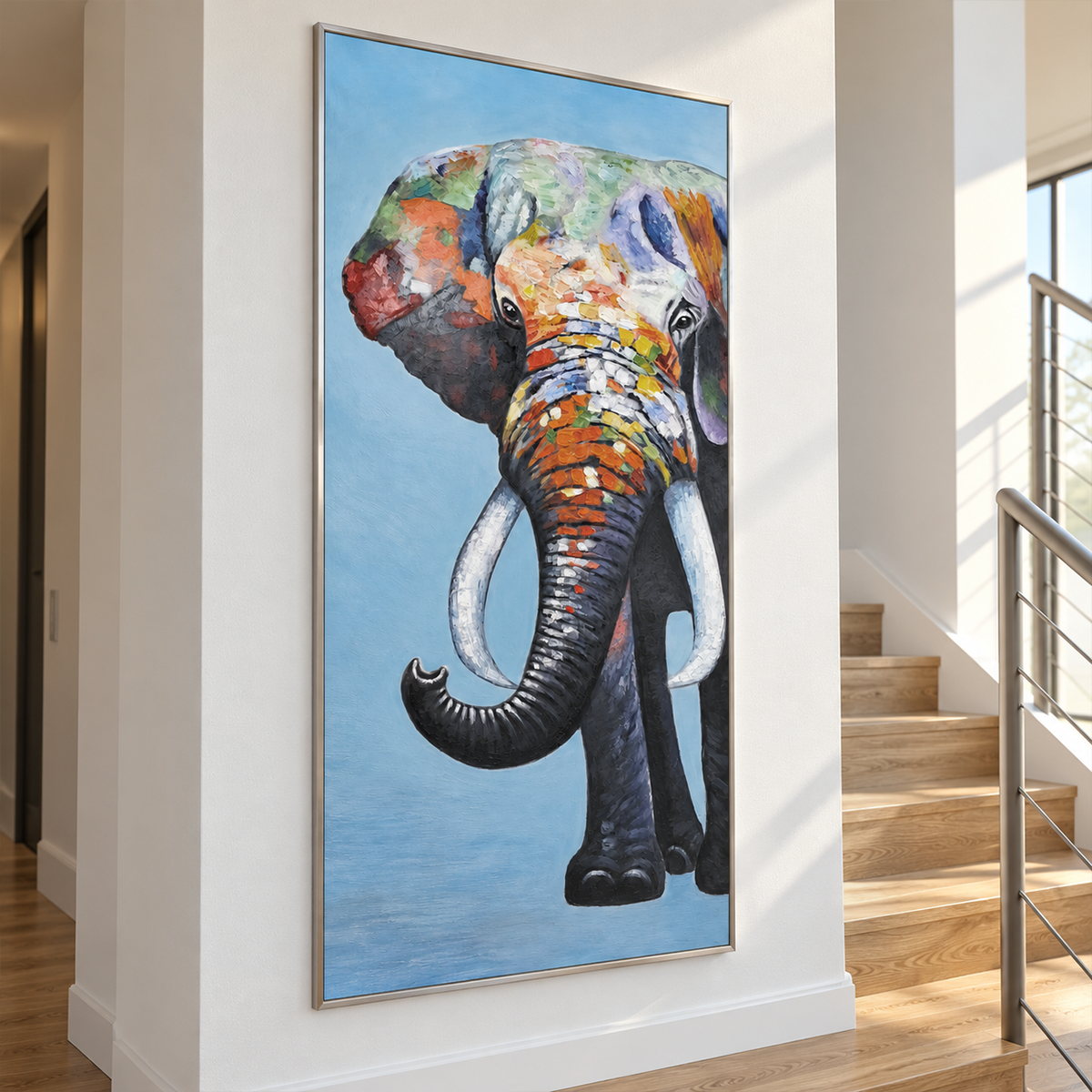 Beside a staircase, an artwork with a silver-colored frame shows a front-facing elephant with an upcurled trunk, pale tusks and colored blocks on blue.