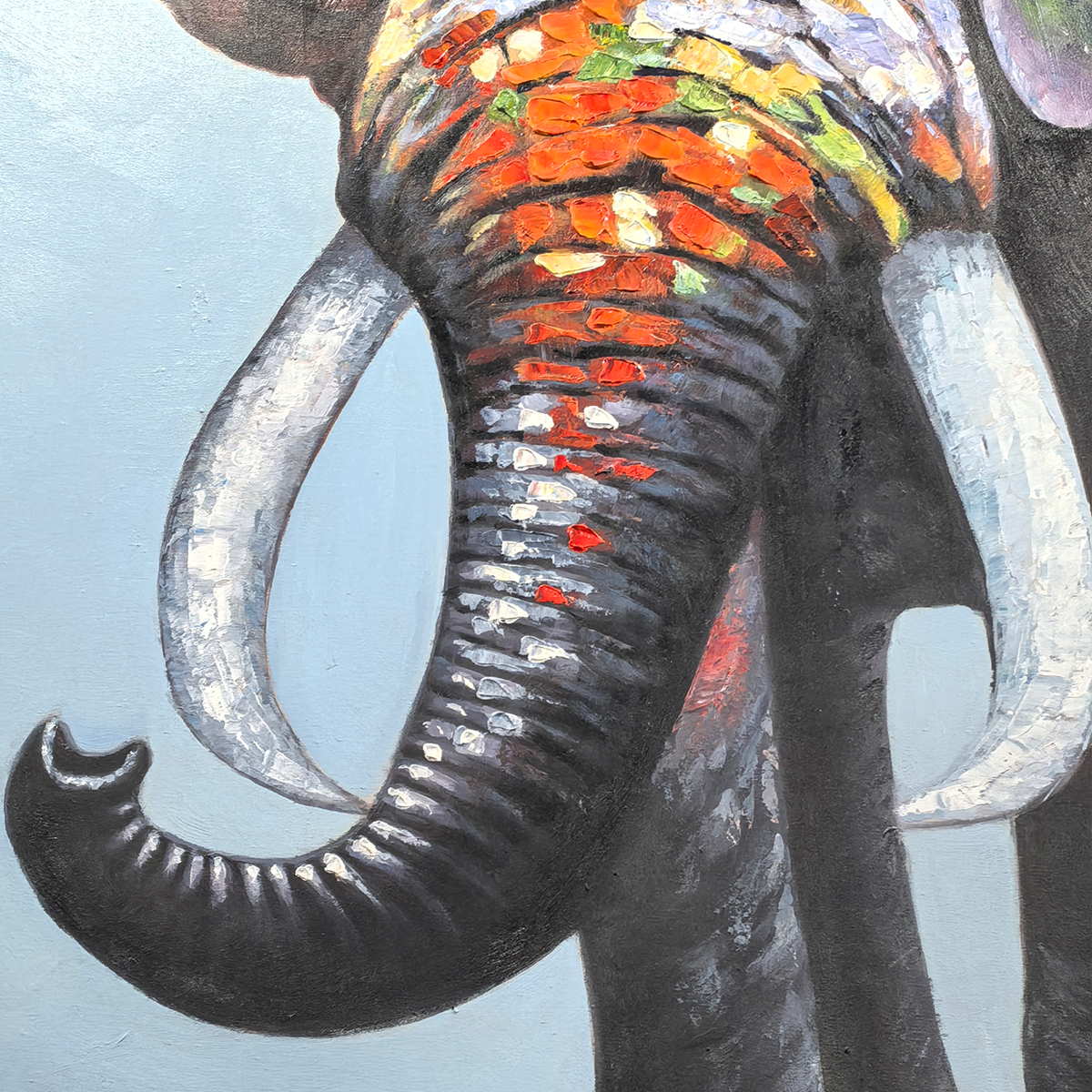 Close-up of the upcurled dark trunk, pale tusks and orange, white and green color blocks.