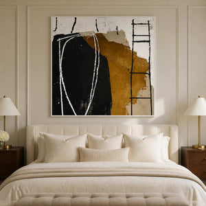 White framed black and ochre artwork above a cream bed between matching bedside lamps.