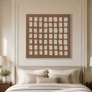 White framed cream grid artwork above a bed with layered ivory pillows.