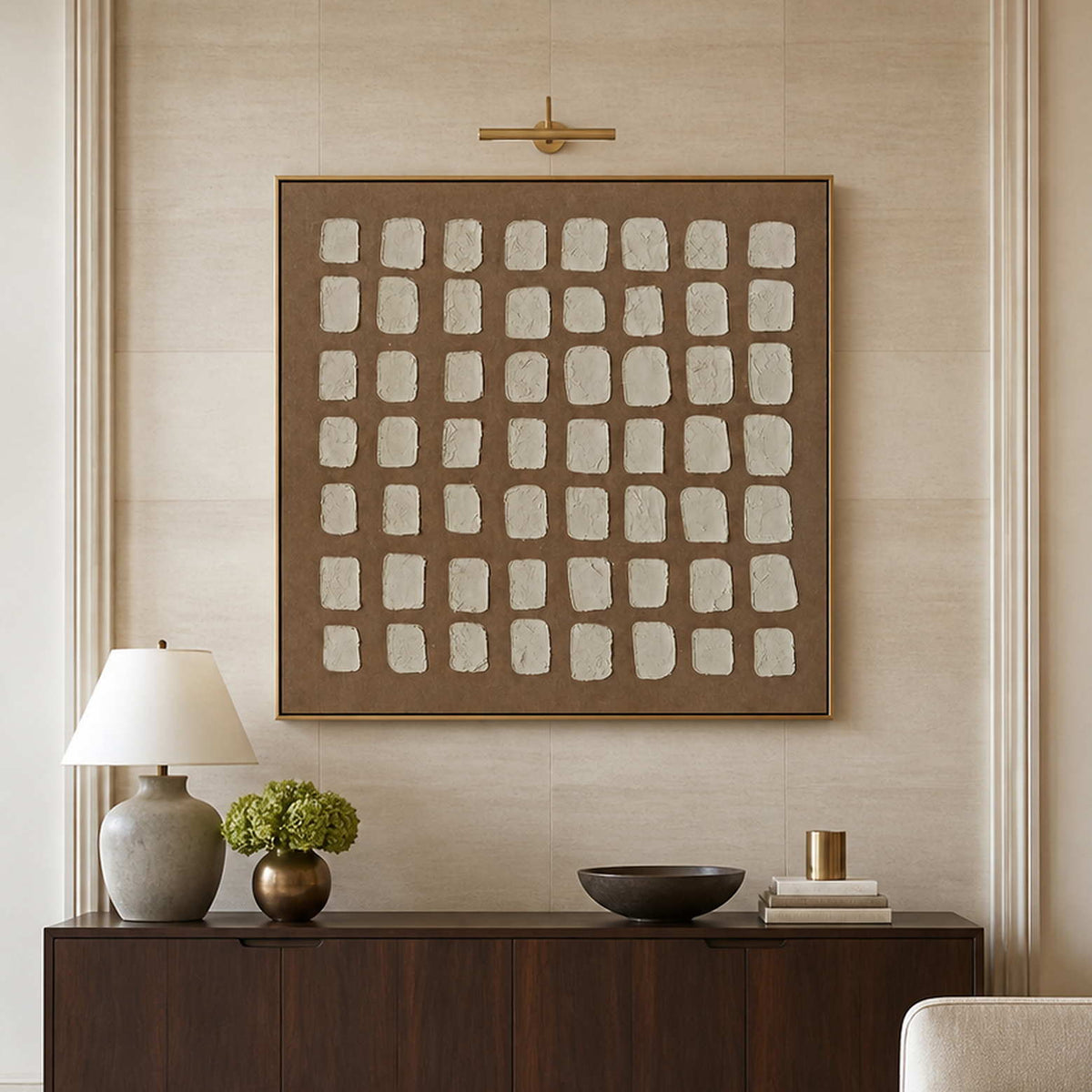 Gold framed cream grid artwork above a hotel lobby sideboard with flowers and books.