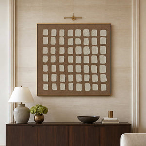Gold framed cream grid artwork above a hotel lobby sideboard with flowers and books.