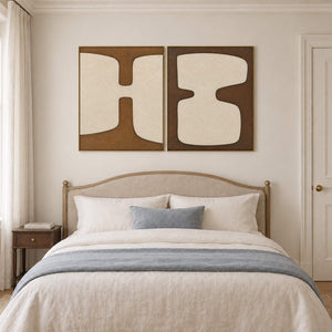 Two panels of complementary ivory organic forms on brown grounds in gold frames, displayed above a bed.