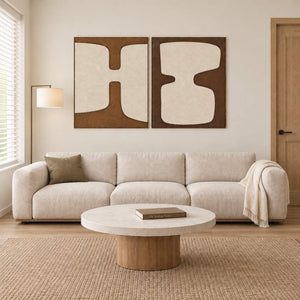 Two panels of complementary ivory organic forms on brown grounds in brown wood frames, displayed above a sofa in a living room.