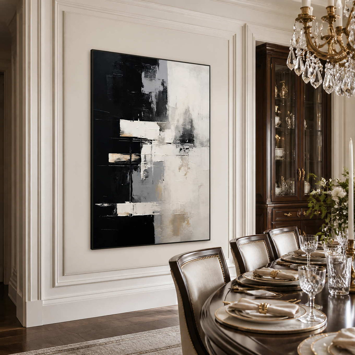 Black framed monochrome abstract artwork beside a dining table under a crystal chandelier.