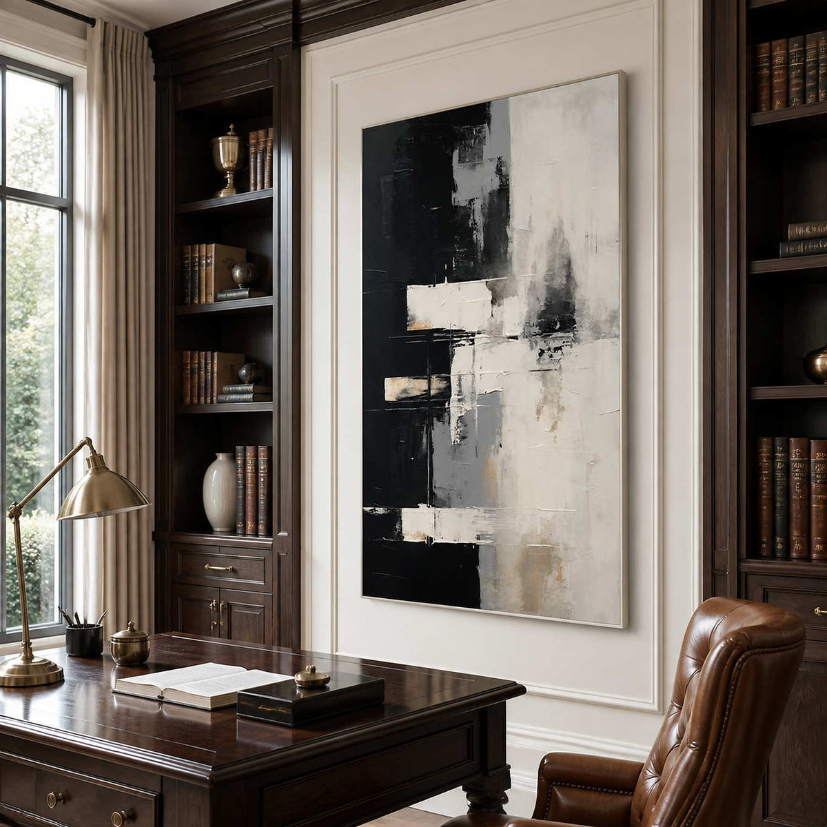 Silver framed monochrome abstract artwork above a wooden desk between dark library shelves.