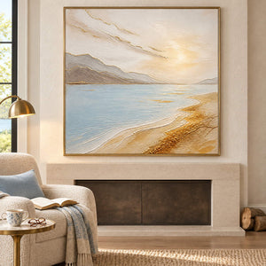 Coastal painting with pale blue water, golden sand, and distant hills in a gold frame in a seating area beside a fireplace.