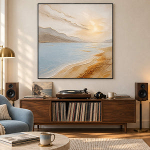 Coastal painting with pale blue water, golden sand, and distant hills in a black frame in a music listening room.