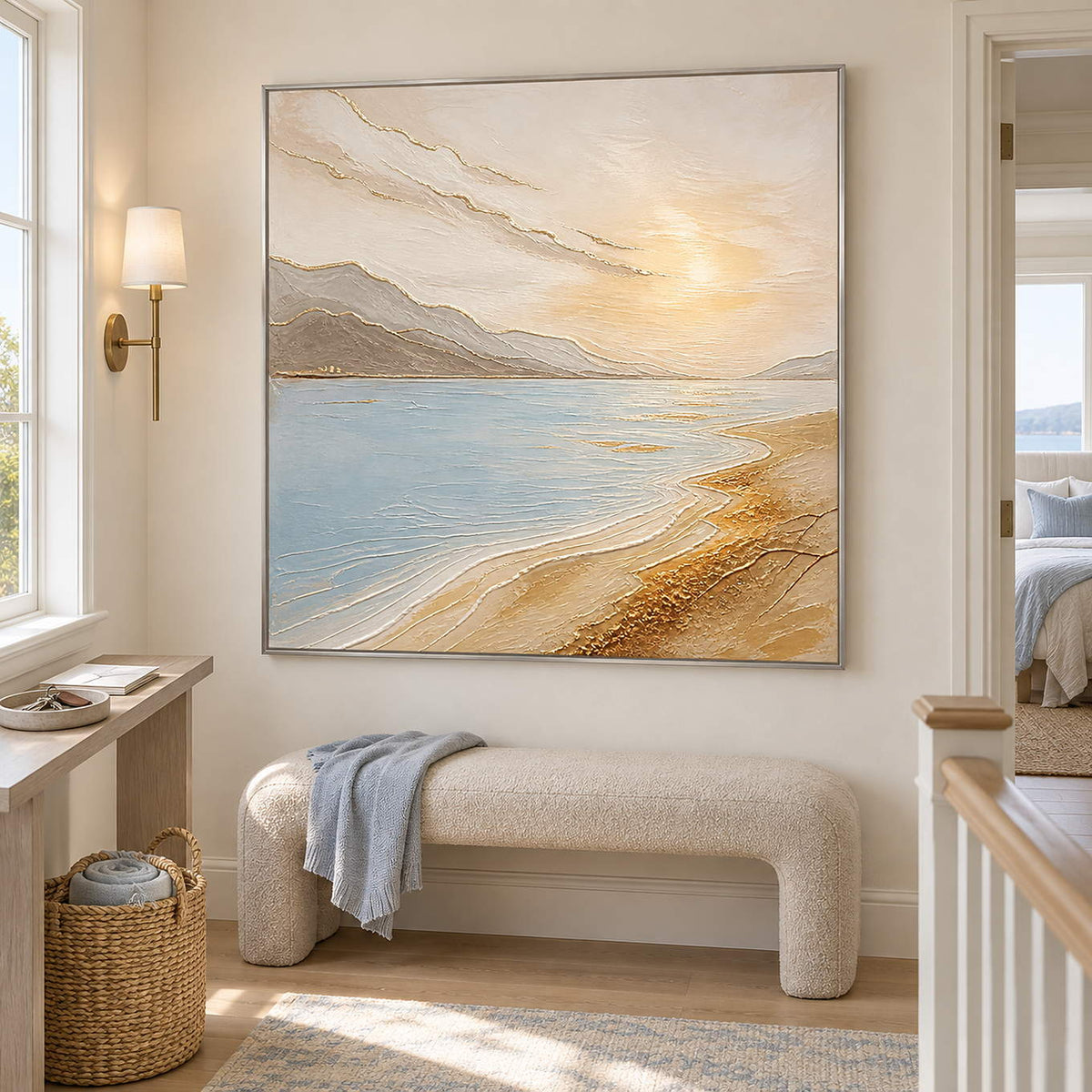 Coastal painting with pale blue water, golden sand, and distant hills in a silver frame on a stair landing.