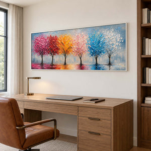 A row of colorful trees reflected beneath a pale sky in a white frame, displayed in a home office.