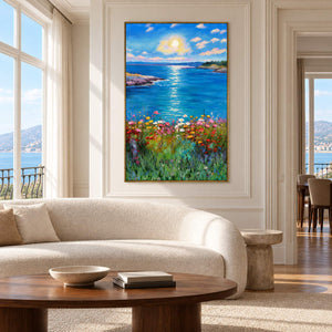 Artwork showing a sunlit blue sea between low shores with colorful flowers in the foreground in a living room above seating, with a gold-colored frame.