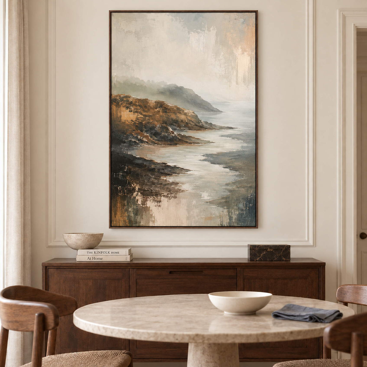 A rocky coast receding into soft gray mist in a brown wood frame, displayed above a dining table.