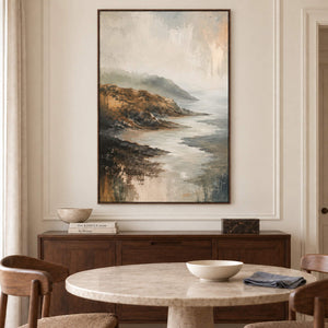 A rocky coast receding into soft gray mist in a brown wood frame, displayed above a dining table.