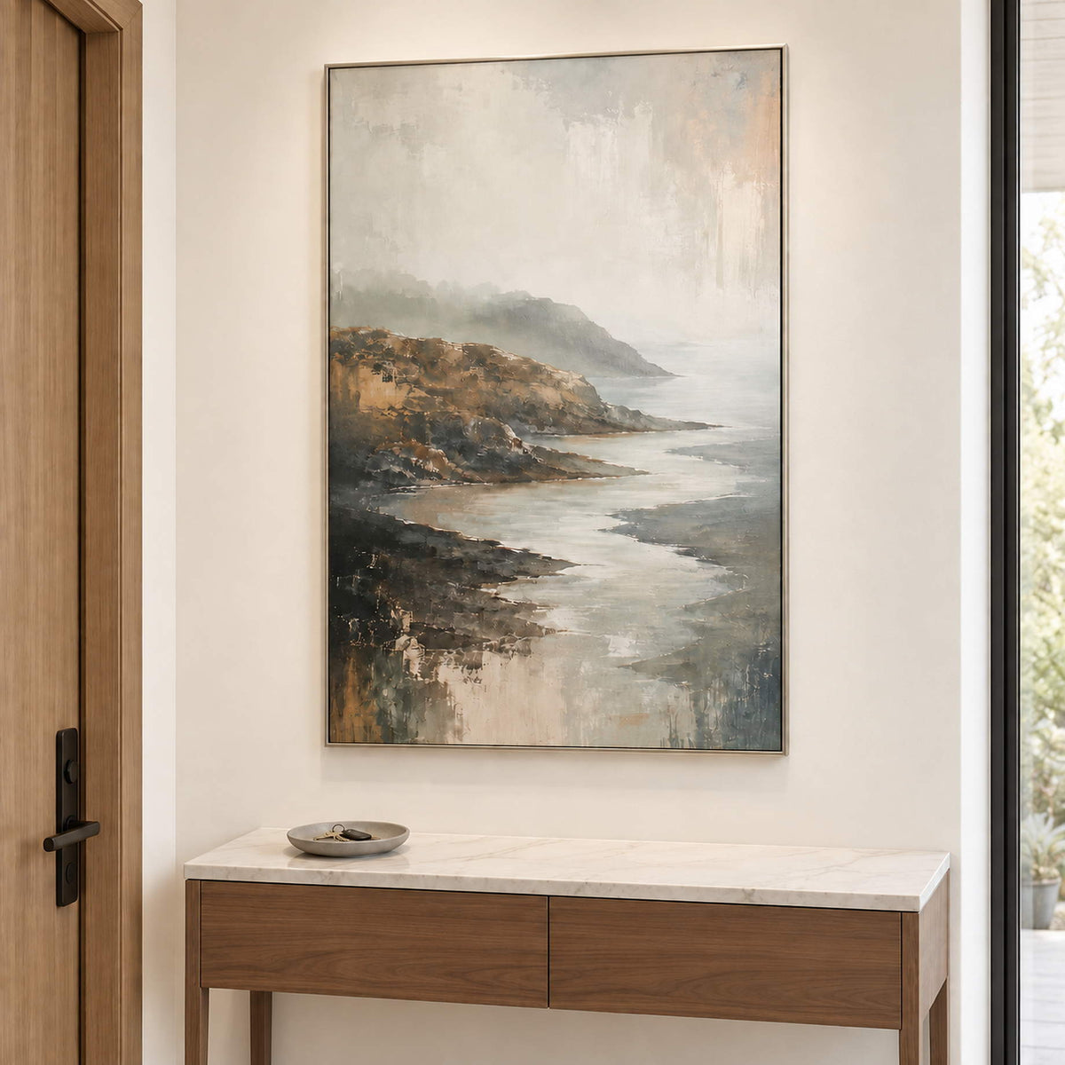 A rocky coast receding into soft gray mist in a silver frame, displayed above an entryway console.