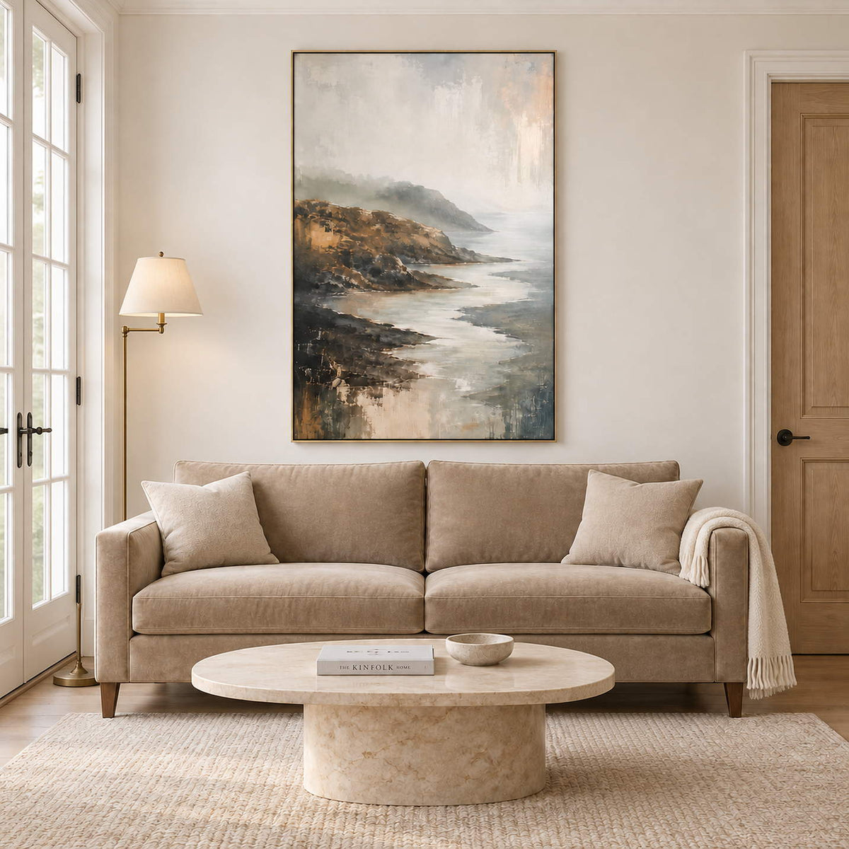 A rocky coast receding into soft gray mist in a gold frame, displayed above a sofa in a living room.