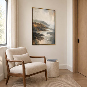 A rocky coast receding into soft gray mist in a gold frame, displayed beside seating in a lounge.