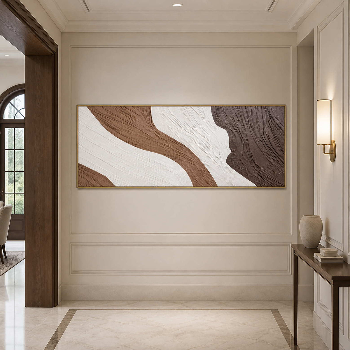 Gold-framed textured abstract wall art on a paneled hallway wall beside a sconce.