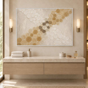 Ivory relief painting with crossing bands of gold and cream circles in a white frame beside a bathroom vanity.