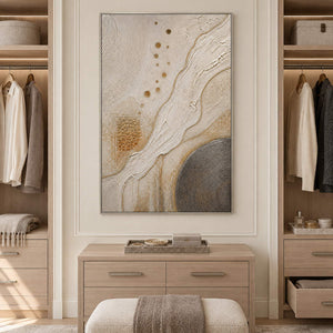 Ivory and gold relief painting with flowing ridges and textured circles in a silver frame in a dressing area.