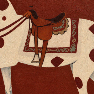 Close view of the brown saddle, patterned saddlecloth, and cream spotted horse.