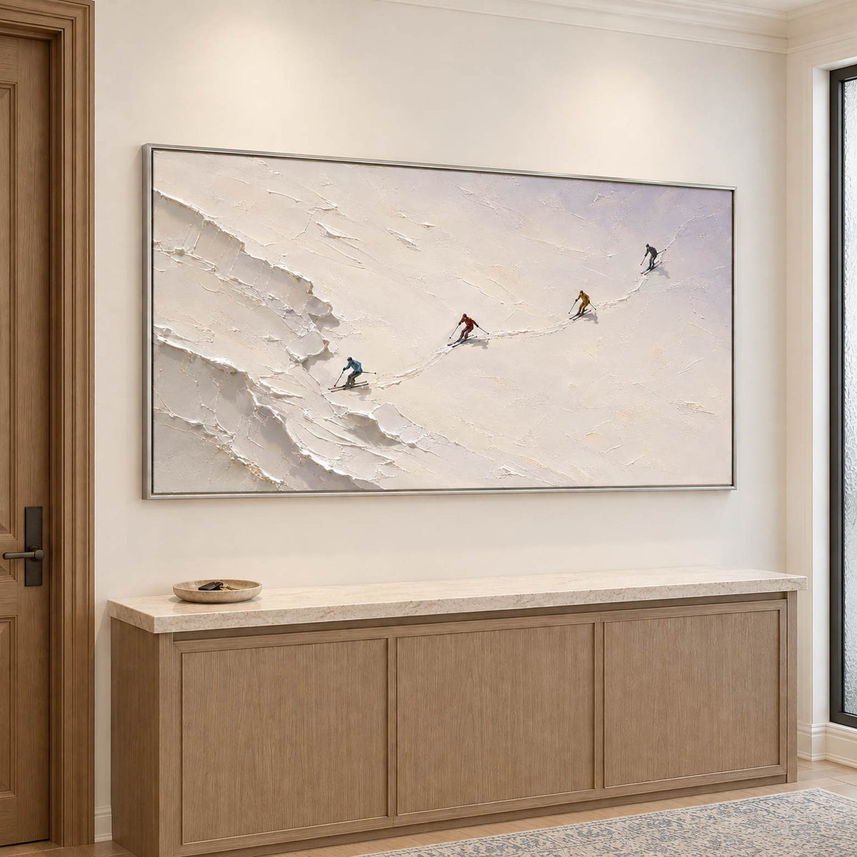 Four skiers crossing an open ivory-white slope in a silver frame, displayed above an entryway console.
