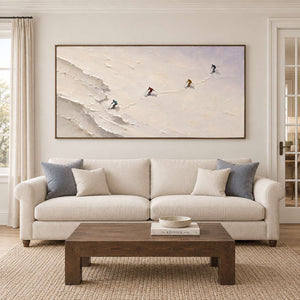 Four skiers crossing an open ivory-white slope in a brown wood frame, displayed above a sofa in a living room.