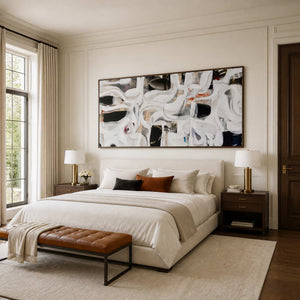 Wood framed panoramic abstract artwork above a cream bed with contrasting accent cushions.