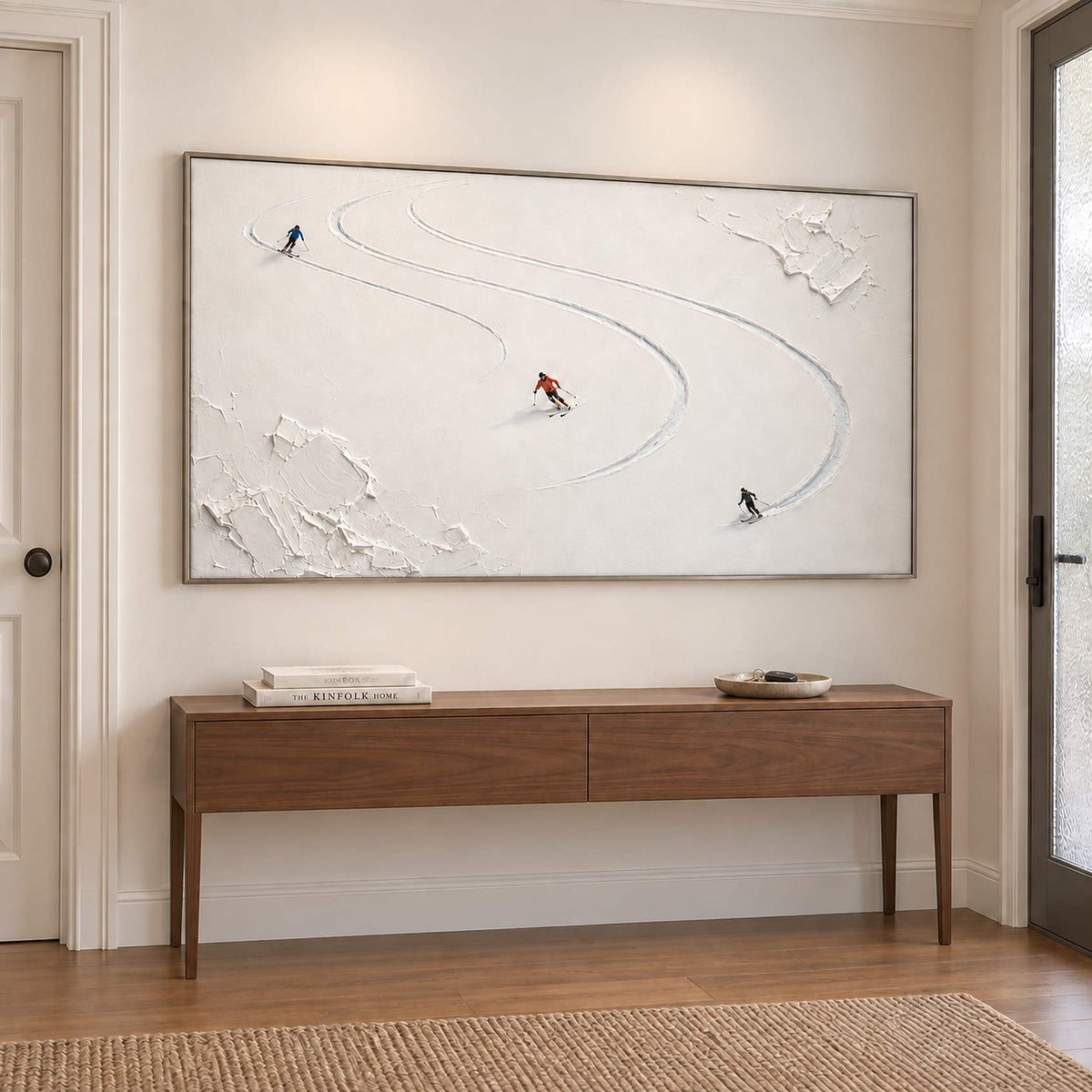 Three skiers tracing curved tracks through fresh white snow in a silver frame, displayed above an entryway console.