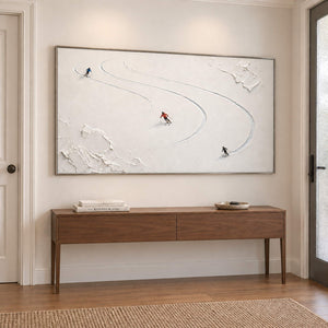 Three skiers tracing curved tracks through fresh white snow in a silver frame, displayed above an entryway console.