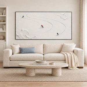 Three skiers tracing curved tracks through fresh white snow in a black frame, displayed above a sofa in a living room.