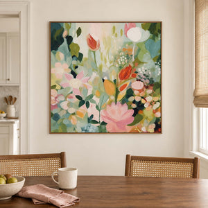 Pink, white and orange flowers among loose green leaves in a brown wood frame, displayed above a dining table.