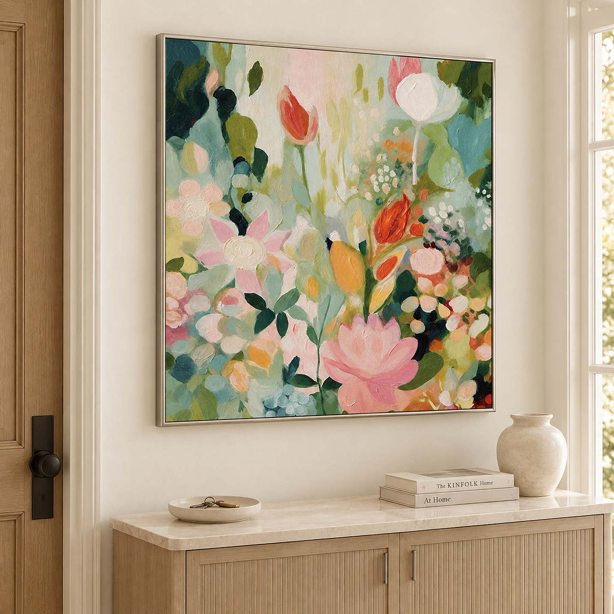 Pink, white and orange flowers among loose green leaves in a silver frame, displayed above an entryway console.
