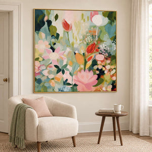 Pink, white and orange flowers among loose green leaves in a gold frame, displayed beside seating in a lounge.