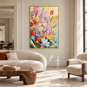 Purple flowers, red cup-shaped blooms and blue-white sprays on yellow in an artwork with a gold-colored frame, displayed in a living room above seating.