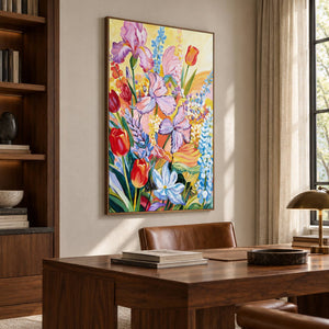 Purple flowers, red cup-shaped blooms and blue-white sprays on yellow in an artwork with a brown wood-look frame, displayed in a study with a desk.