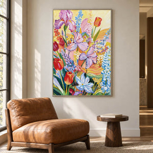 Artwork showing purple flowers, red cup-shaped blooms and blue-white sprays on yellow beside a reading chair, with a silver-colored frame.