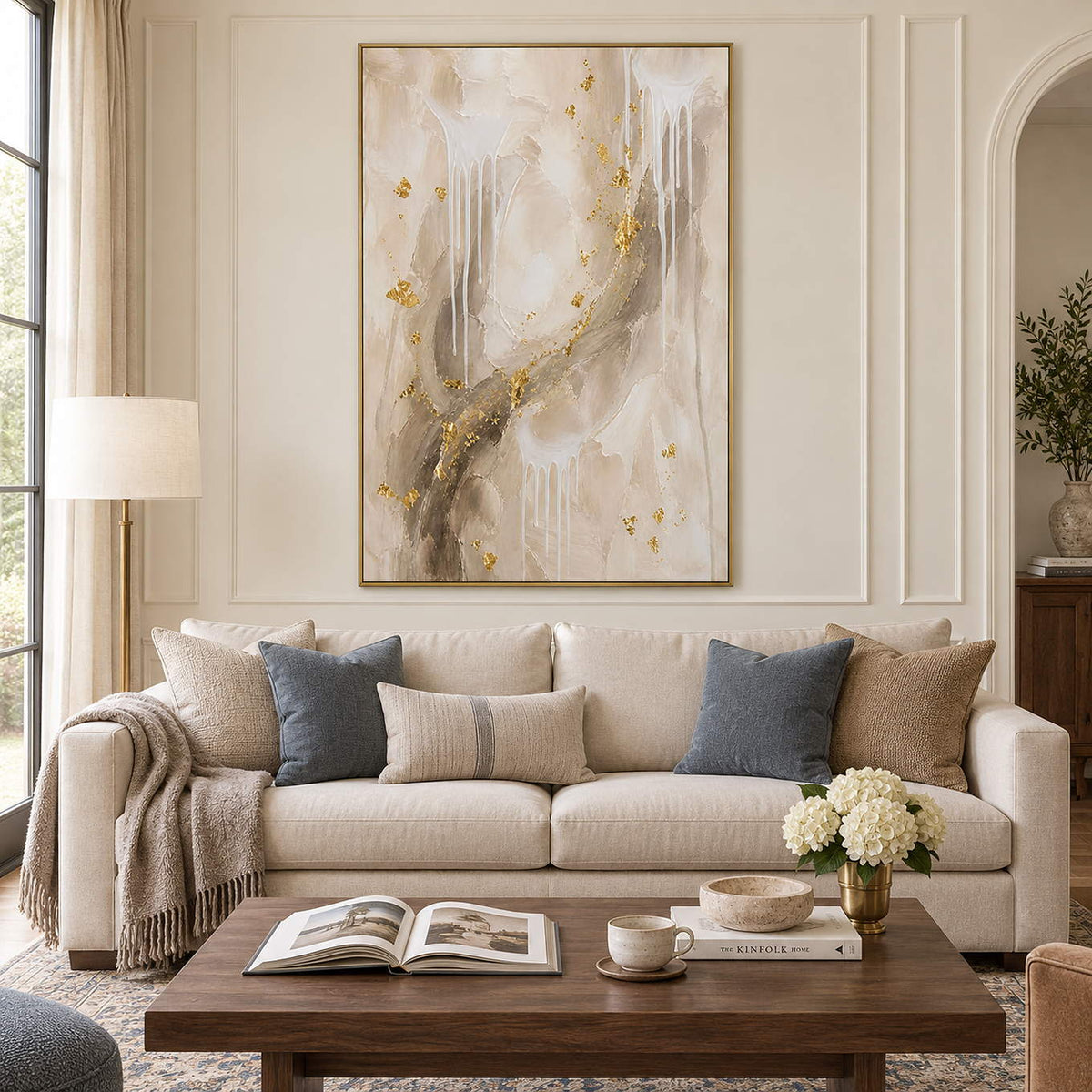 Ivory and taupe abstract painting with white drips and gold accents in a gold frame in a living room.