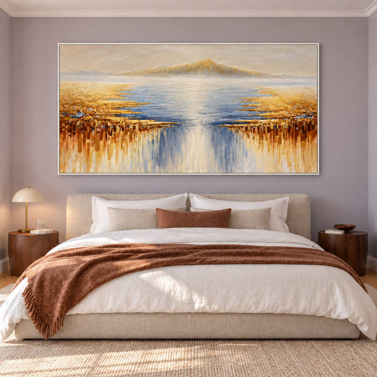 Pale distant mountains above blue-gray water and gold-ochre marks spreading from both sides in an artwork with a white frame, displayed in a bedroom near the bed.