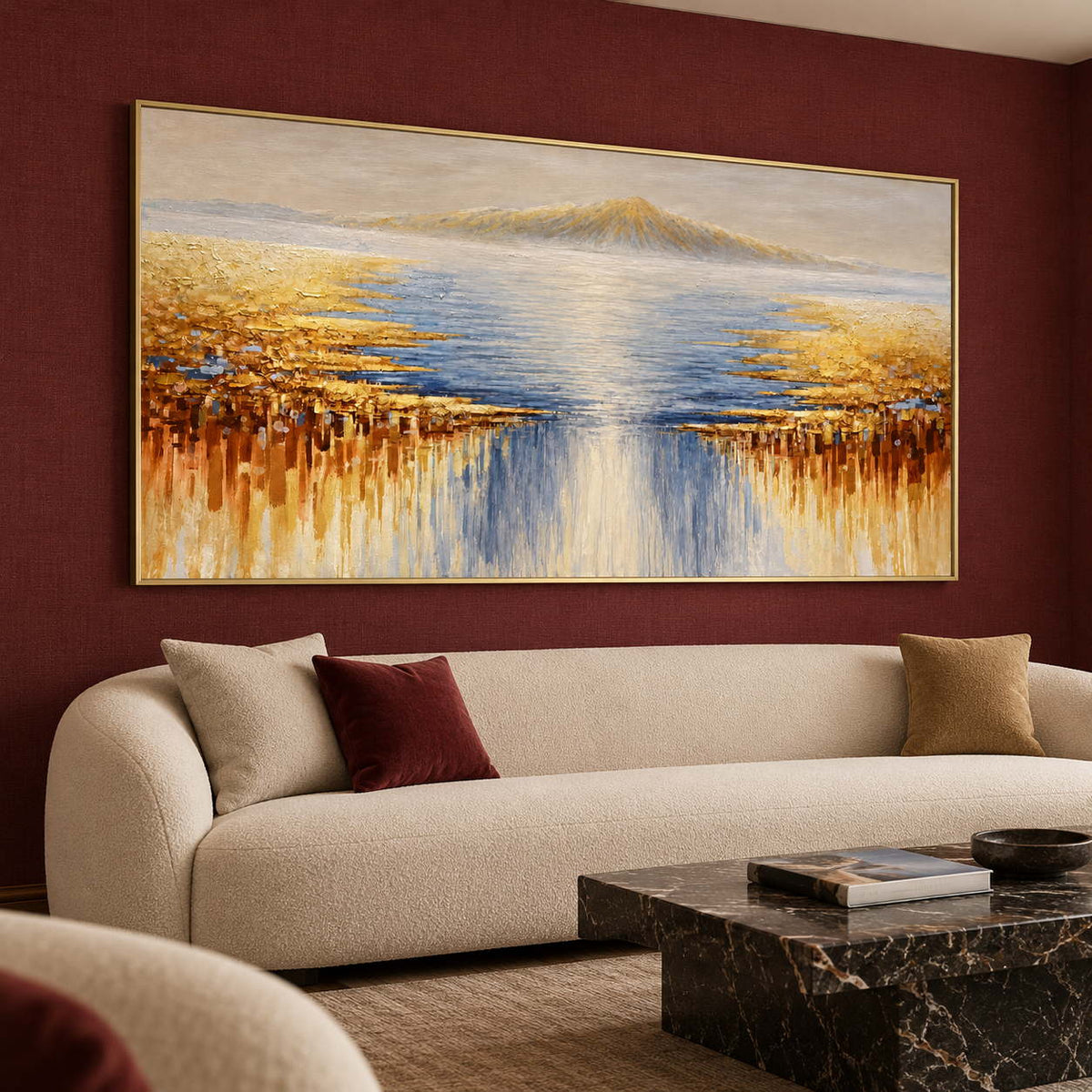 Pale distant mountains above blue-gray water and gold-ochre marks spreading from both sides in an artwork with a gold-colored frame, displayed in a seating area.