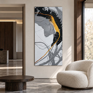 Broad black and gray brush arcs crossed by a gold-colored line and white flecks in an artwork with no outer frame, displayed in a seating area.