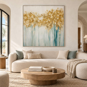 Hand-painted gold blossoms above soft aqua and ivory drips on canvas, displayed in a living room in a silver frame.